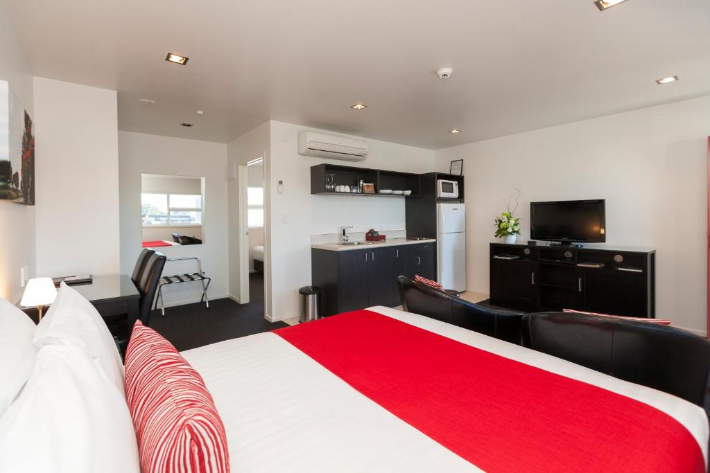 a bedroom with a red and white bed and a kitchen at The Dawson Motel in New Plymouth