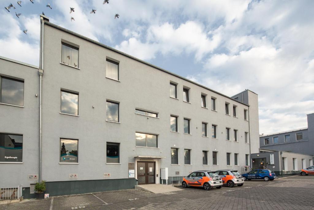 un grand bâtiment blanc avec des voitures garées dans un parking dans l'établissement T3 Hotel Cityloft, à Mönchengladbach