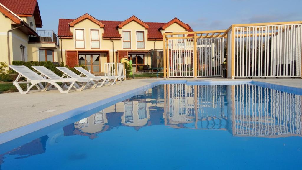 a swimming pool with lounge chairs next to a house at Koralia Domki i Apartamenty in Sarbinowo