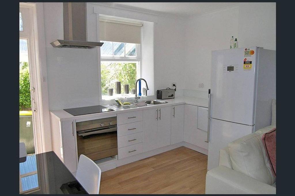 a white kitchen with a refrigerator and a sink at Hobart Colonial Apartment in Hobart