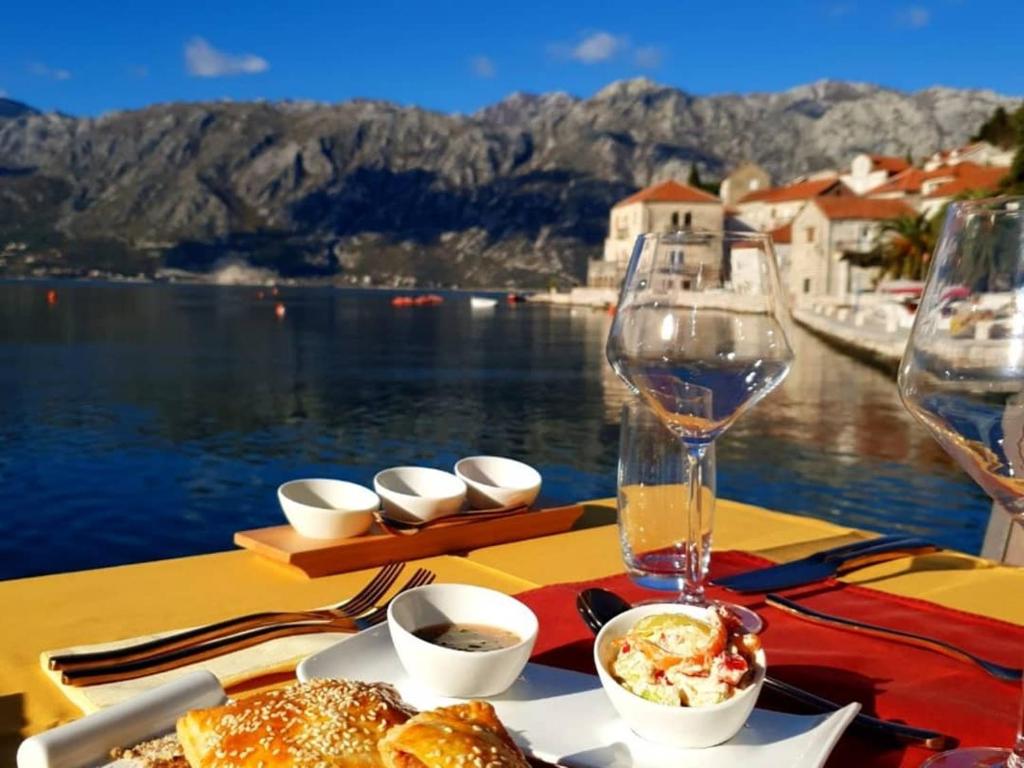una tavola con un piatto di cibo e un bicchiere di vino di Apartmani Armonia a Perast