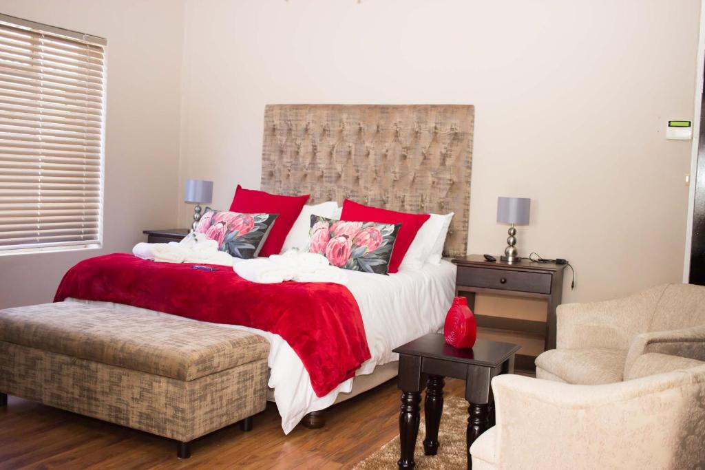 a bedroom with a bed with red pillows and a chair at Heimat Guesthouse in Welkom
