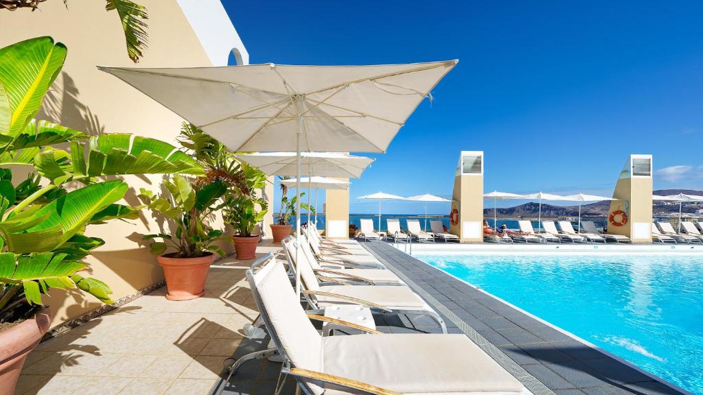 a pool with white chairs and umbrellas on a resort at Bull Reina Isabel & SPA in Las Palmas de Gran Canaria