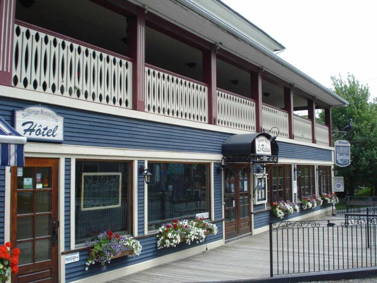 - un bâtiment avec une terrasse couverte et des fleurs devant dans l'établissement AUBERGE Knowlton, à Lac-Brome