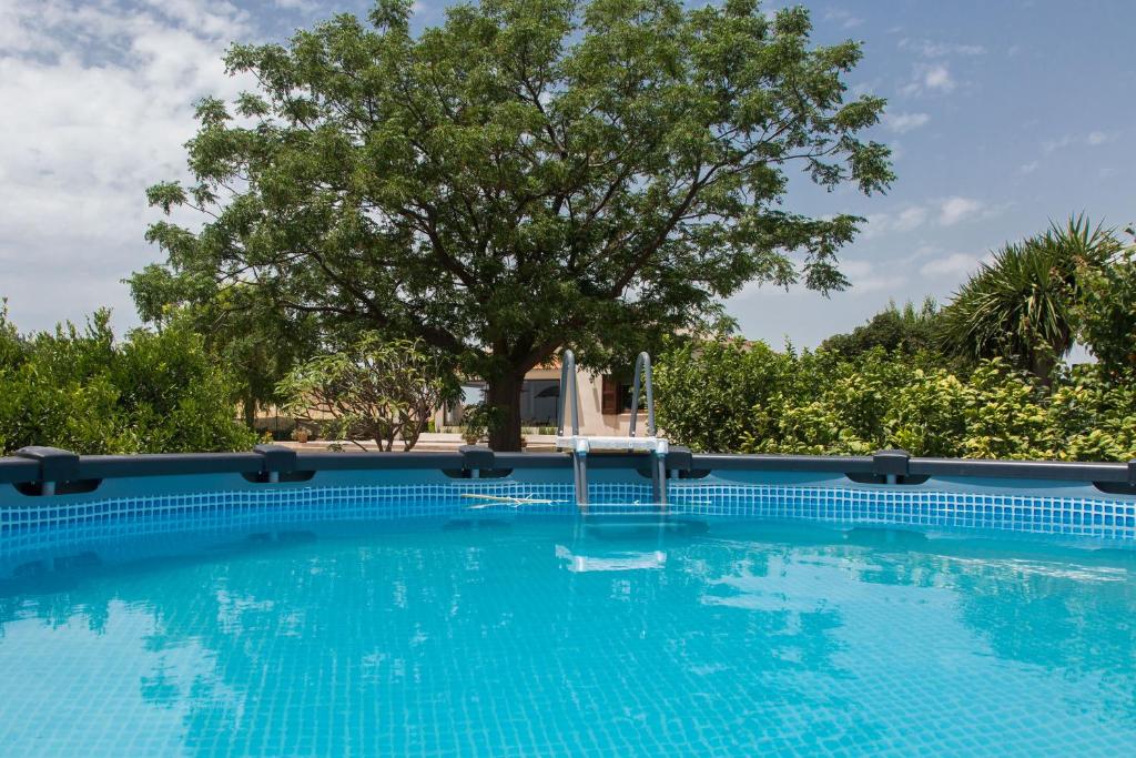 ein großer blauer Pool mit einem Baum im Hintergrund in der Unterkunft Villa Ammaliante in Menfi