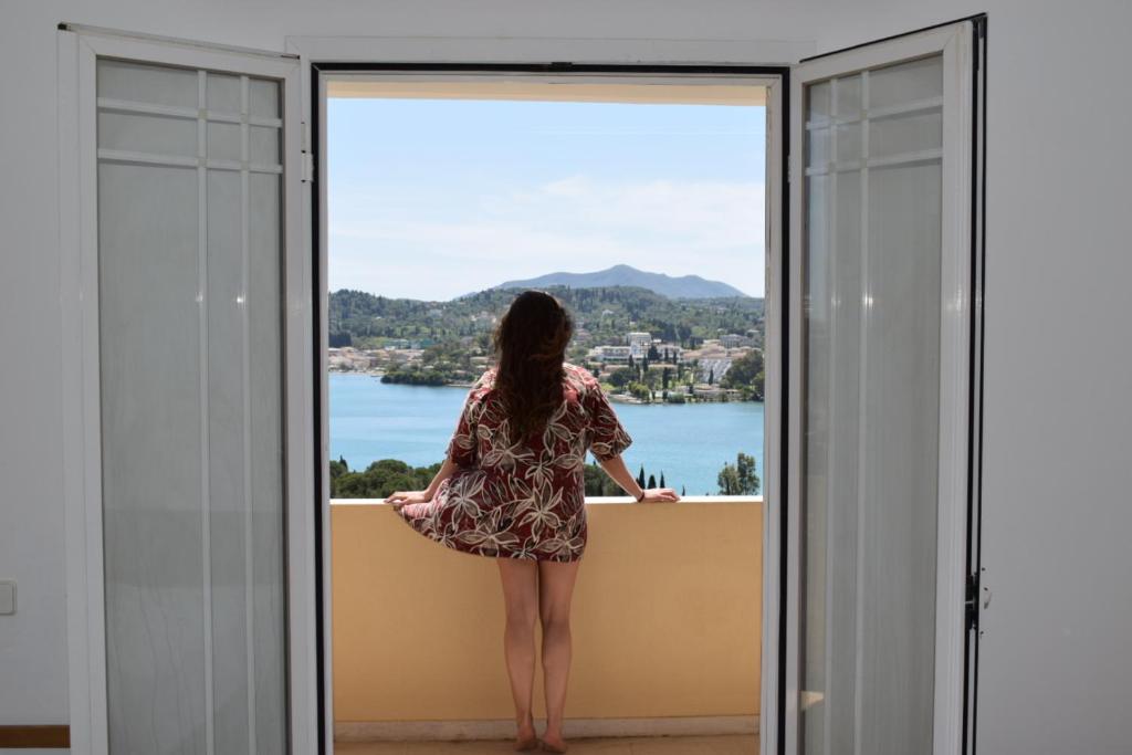 Eine Frau steht auf einem Balkon mit Blick aus dem Fenster in der Unterkunft Elite Corfu Sea View Rooms in Korfu-Stadt