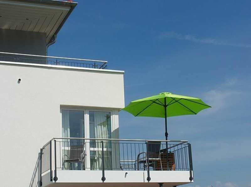 a balcony with a green umbrella and chairs on it at Apartmentvermittlung Mehr als Meer - Objekte 42 & 51 in Niendorf