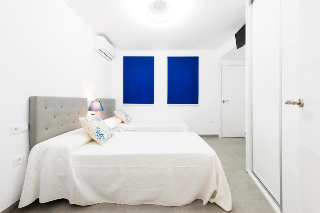 um quarto branco com janelas azuis e uma cama em EDIFICIO SUR em Nerja