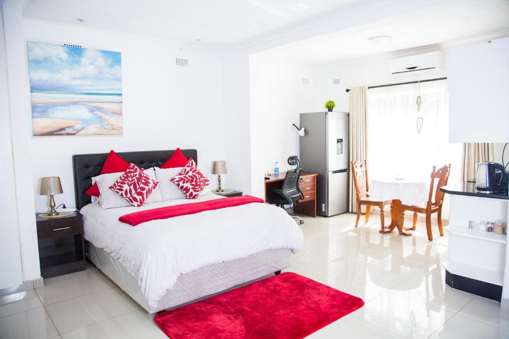 a white bedroom with a large bed with red pillows at Mt Pleasant B'n'B in Harare