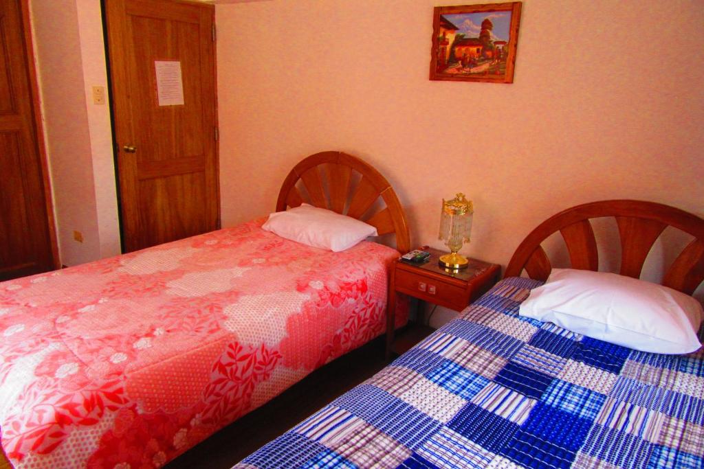 a bedroom with two beds and a table with a night stand at Hospedaje Kamila in Cusco