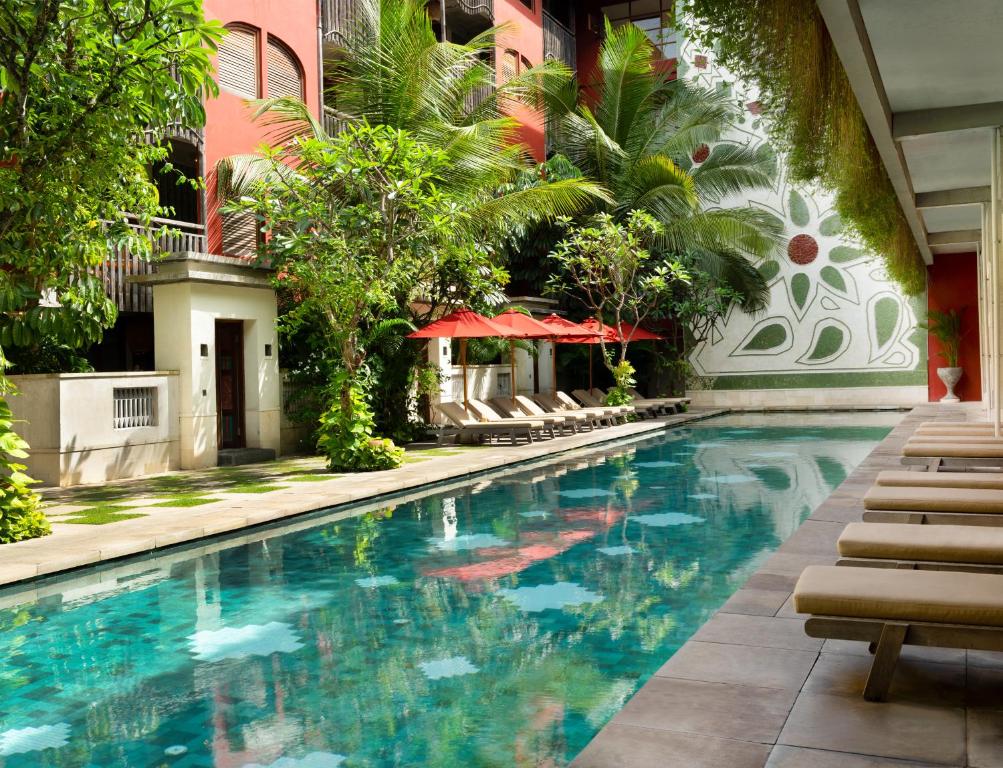 a swimming pool in front of a building with chairs and trees at Amnaya Resort Kuta in Kuta