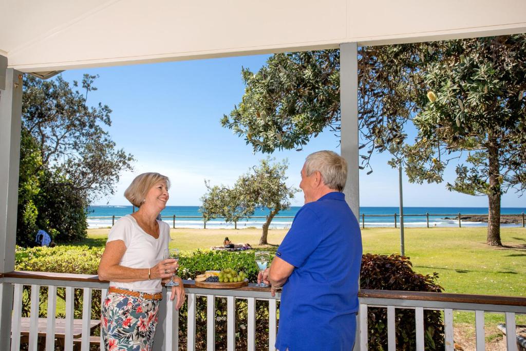 Una pareja mayor parada en un porche con vistas a la playa en Woolgoolga Beach Holiday Park en Woolgoolga