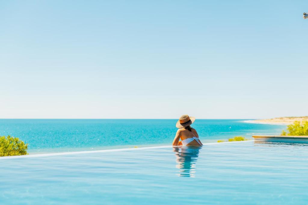una mujer sentada en una piscina infinita mirando al océano en Eco Beach Wilderness Retreat en Broome