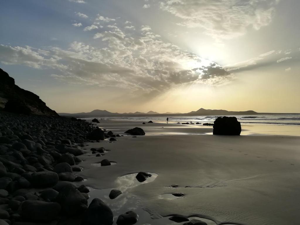a beach with the sun setting on the sand at El Charquito in Famara