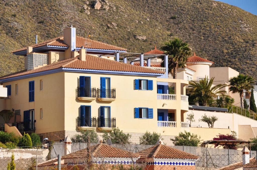 a large yellow house with blue windows and a hill at Hotel Mayarí in Calabardina