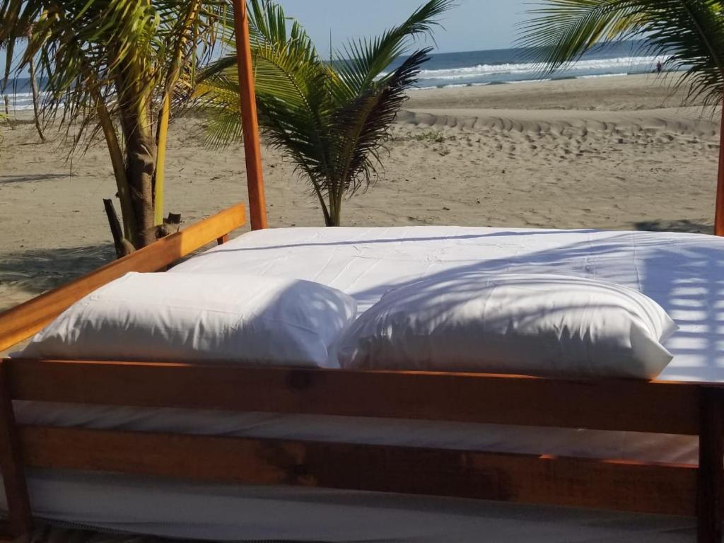 a bed with white pillows sitting on a beach at Nichos Beach Villas in Playa Azul