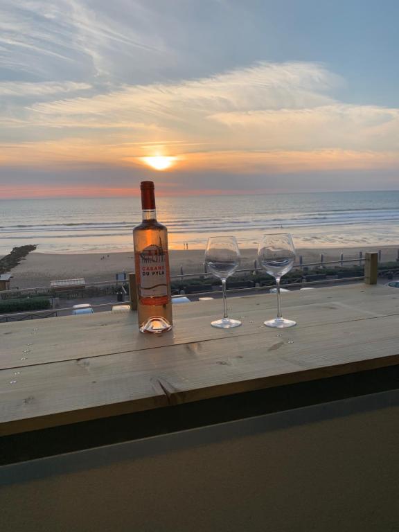 a bottle of wine and two glasses on a table with the beach at LACANAU FRONT DE MER in Lacanau