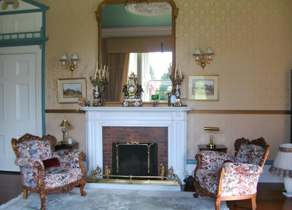 a living room with a fireplace with two chairs and a mirror at Gardenvale Manor House B&B in Stranocum