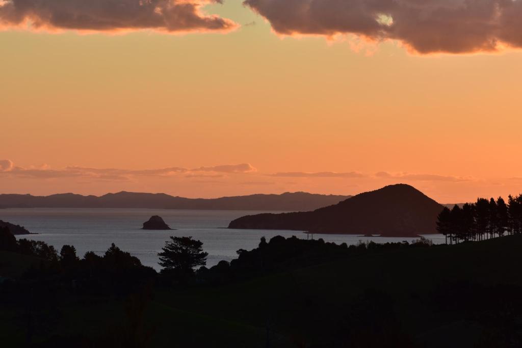 a sunset over the ocean with mountains in the background at Atea Lodge in Coromandel Town
