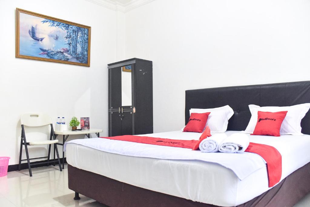 RedDoorz near Sultan Hasanuddin Airport 2 في ماكاسار: غرفة نوم بسرير كبير ومخدات حمراء وبيضاء