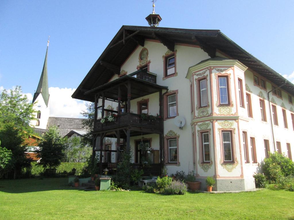 Une grande maison blanche avec une cloche dans la cour dans l'établissement Pension Florian am Park, à Kössen