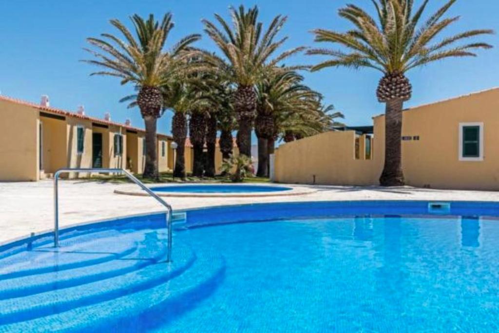 une piscine bordée de palmiers et un bâtiment dans l'établissement Apartamento con piscina y terraza en Ciutadella, Cala en Blanes, à Cala en Blanes