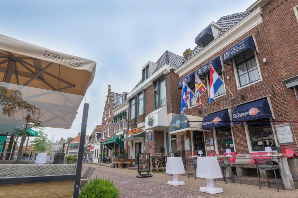 una calle con edificios, mesas y una sombrilla en De Waag, en Makkum