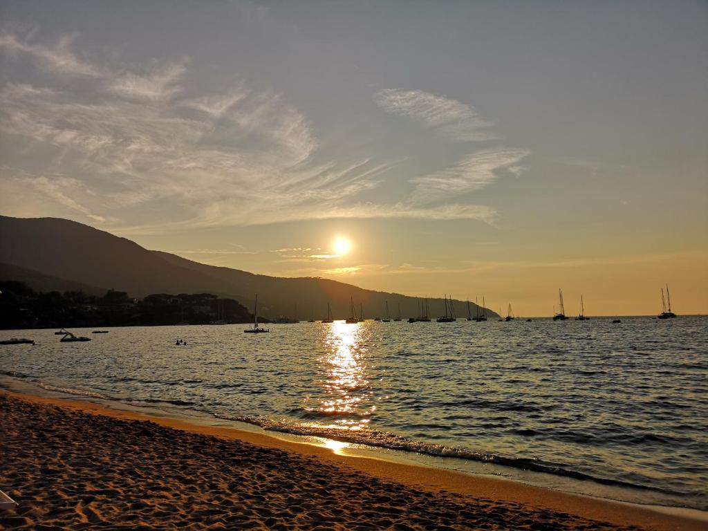 un tramonto sulla spiaggia con barche in acqua di Appartamenti Lucry a Procchio