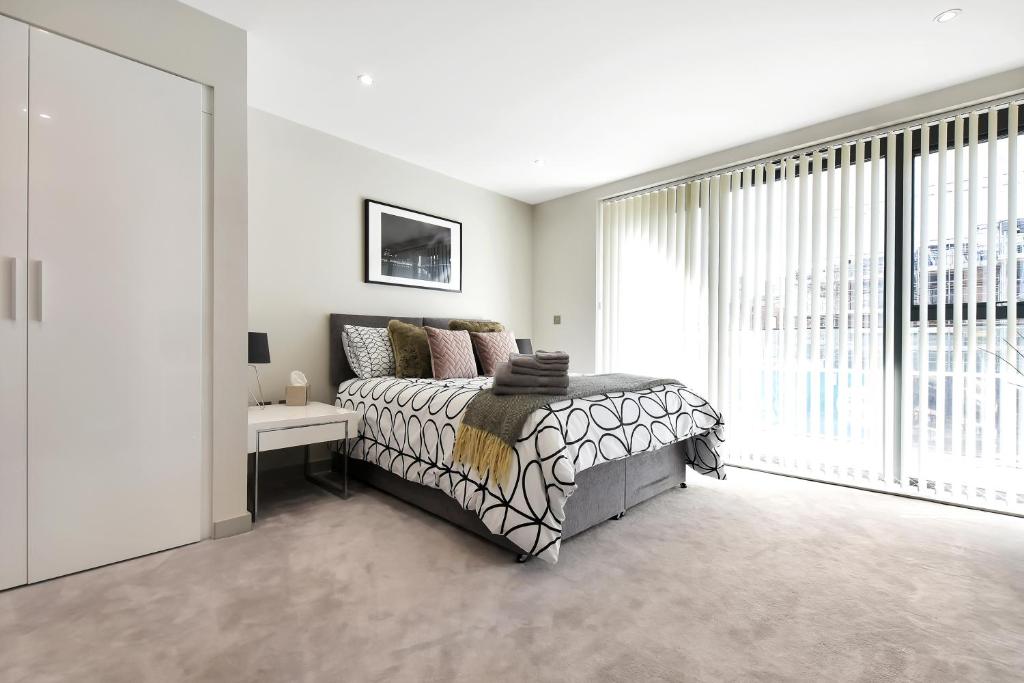 a white bedroom with a bed and a large window at Esquire Apartments Ealing in London