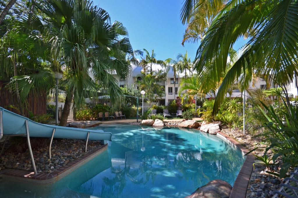 a swimming pool with palm trees in front of a building at Raintrees Moffat Beach in Caloundra