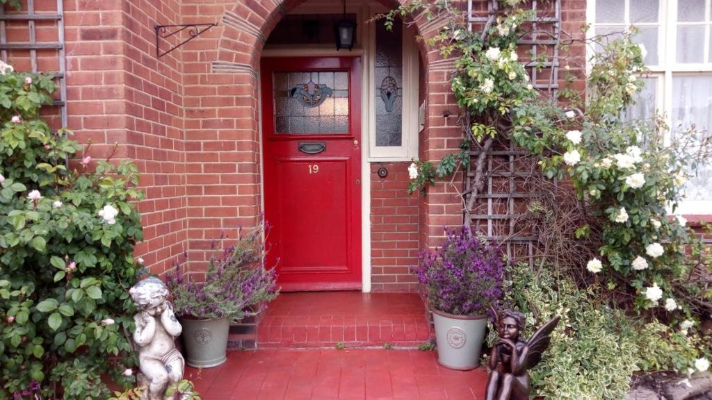 een rode deur op een bakstenen huis met bloemen bij Kingsway Bed & Breakfast in Broxbourne