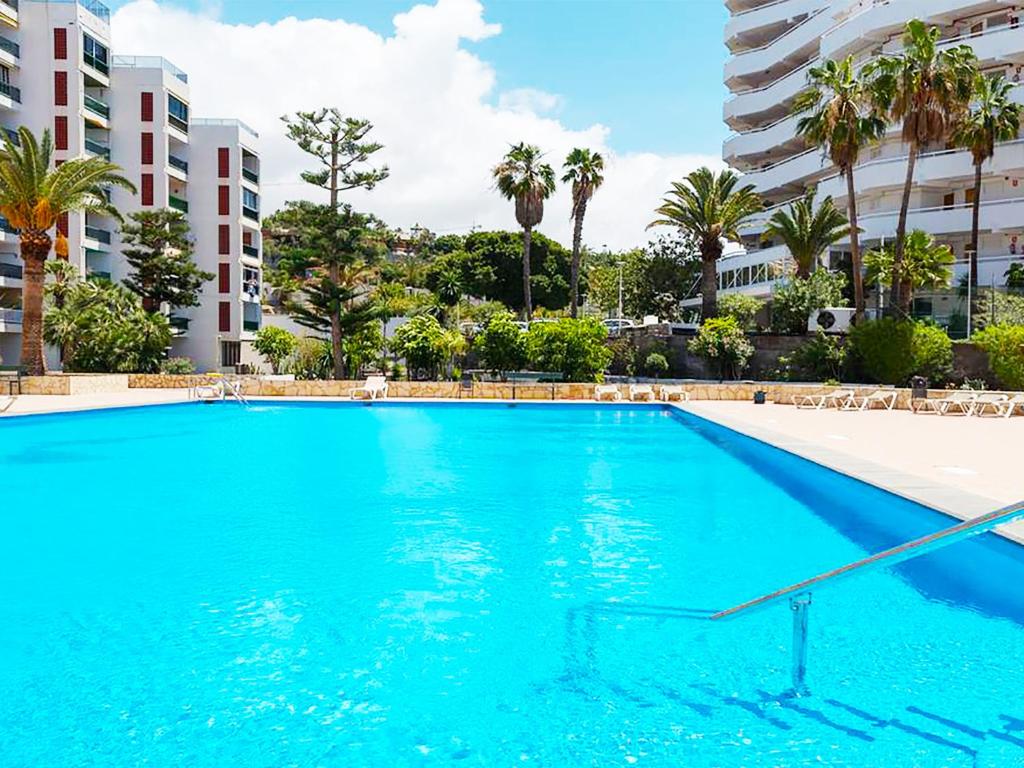 une grande piscine bleue avec des palmiers et des bâtiments dans l'établissement Viñas del Mar with Sea View, à Playa de las Americas