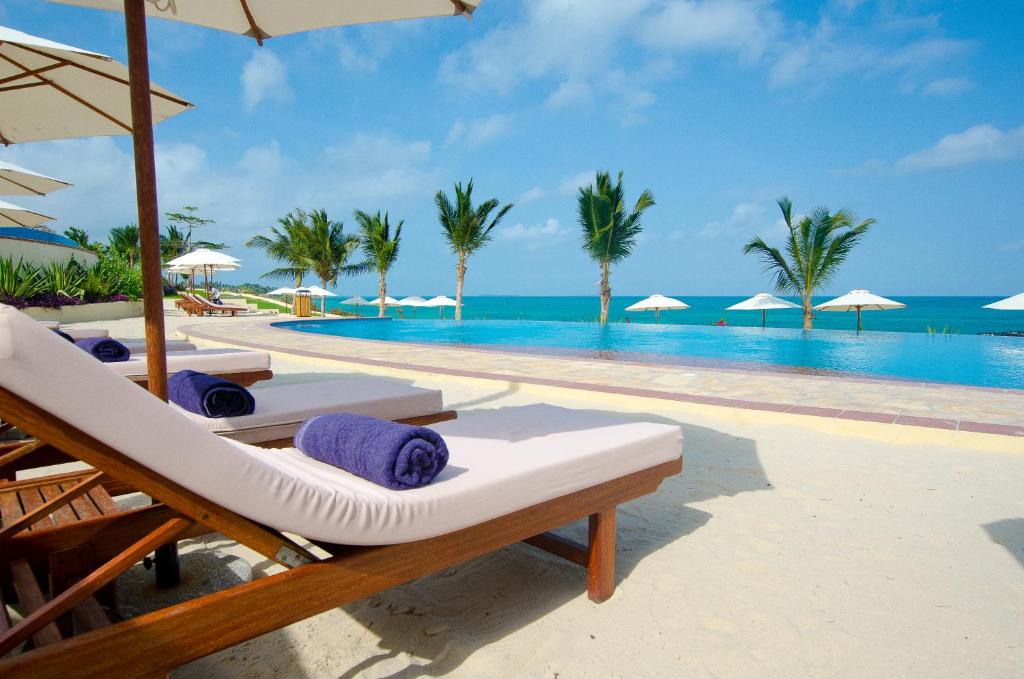 a resort pool with chairs and umbrellas and the ocean at Sea Cliff Resort & Spa in Zanzibar City