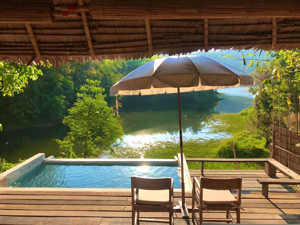 Un patio con dos sillas y una sombrilla junto a una piscina. en Thap Pala Cottage, en Songkhla