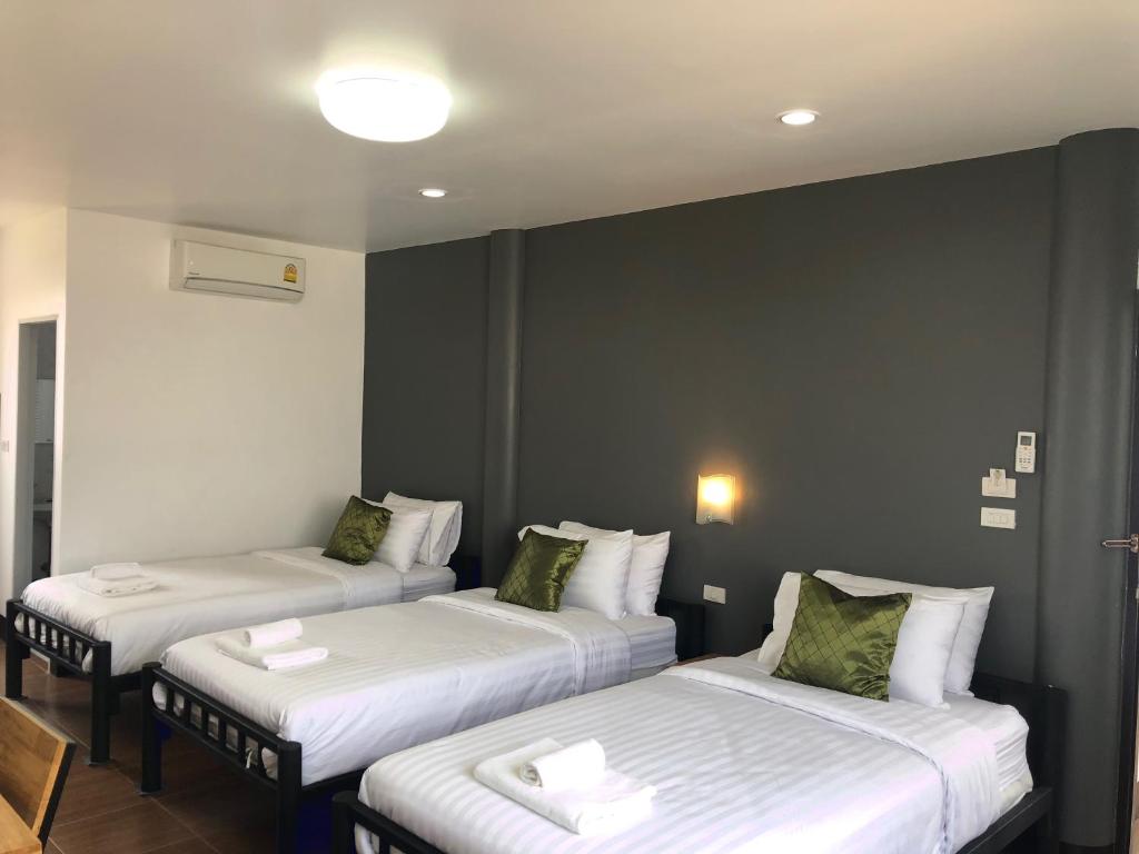 um quarto com 3 camas com lençóis brancos e almofadas verdes em Khaohom House em Chiang Mai