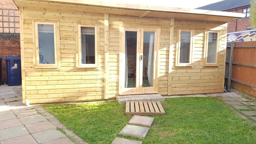 a small wooden house with a porch and grass at Urban Log Cabin near zone 2 tube in London