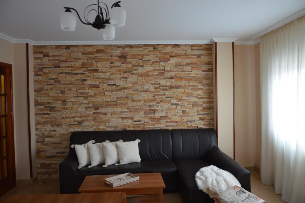 a living room with a black couch and a brick wall at Piso da Empegada in Arzúa