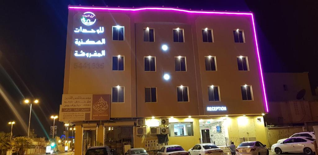 阿爾卡的住宿－Nozul Al Tout Furnished Apartments，一座有照明的建筑,前面有汽车停放