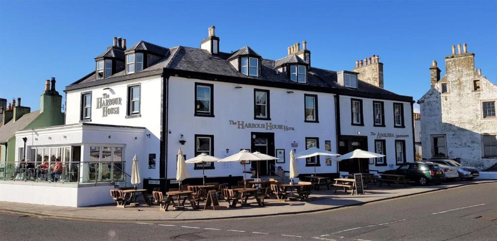 a white building with tables and umbrellas in front of it at The Harbour House Sea front Hotel in Portpatrick