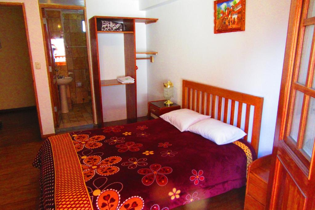 a bedroom with a bed with a red blanket with flowers on it at Hospedaje Kamila in Cusco