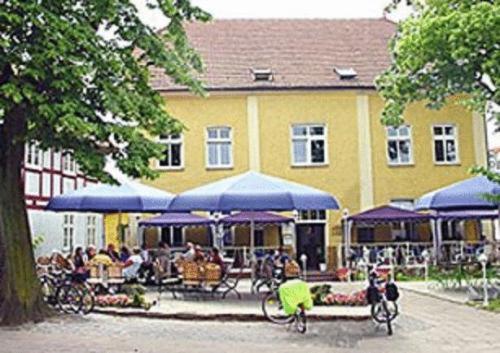 a yellow building with tables and blue umbrellas at Mecklenburger Hof in Mirow
