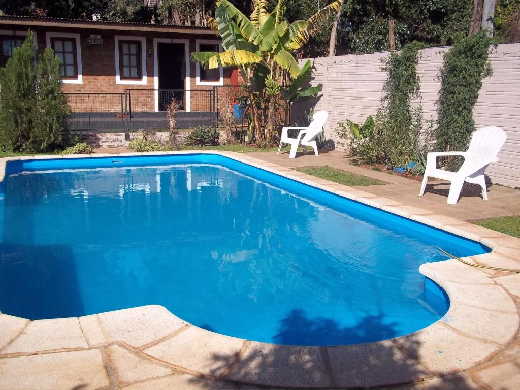 une piscine bleue avec deux chaises et une maison dans l'établissement Posada Iguazu Royal, à Puerto Iguazú