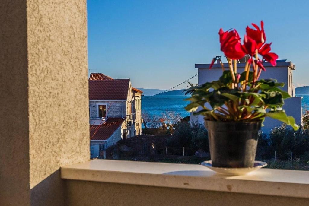 un jarrón con flores rojas sentado en el alféizar de la ventana en apartment by the sea and beach with roof terrace, en Kaštela