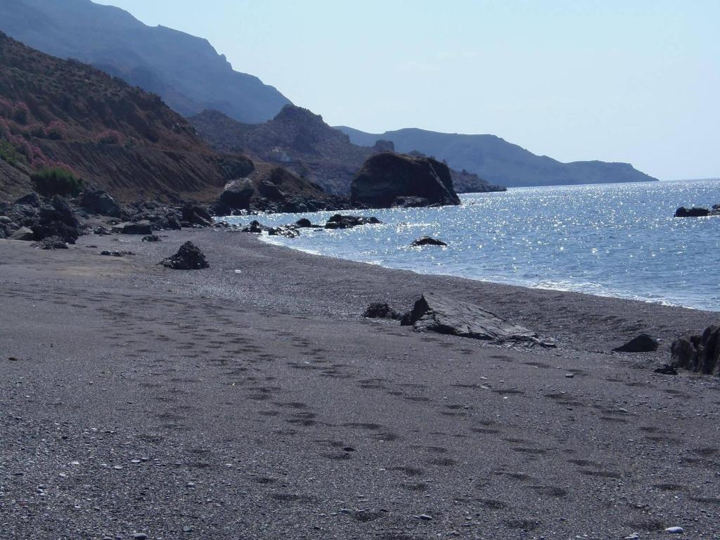 a rocky beach with footprints in the sand and water at House With View in Paránimfoi