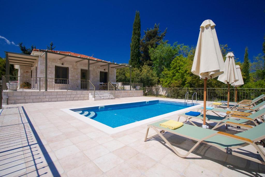 a swimming pool with chairs and an umbrella at Forest Villas Kefalonia in Logaráta