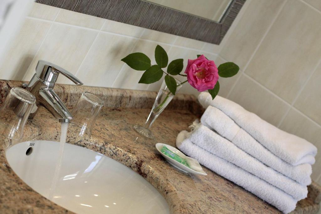 eine Badezimmertheke mit einem Waschbecken und einer Vase mit einer Rose in der Unterkunft Hôtel Maïtagaria in Biarritz