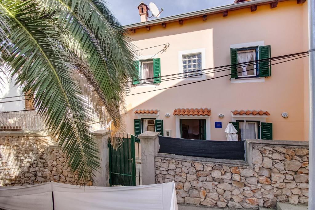 a house with a stone wall and a palm tree at apartman Nataša in Mali Lošinj