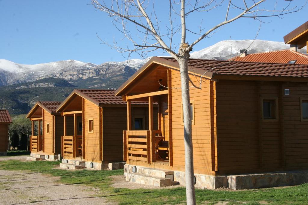 a row of wooden cabins with mountains in the background at Camping Cañones de Guara y Formiga in Panzano