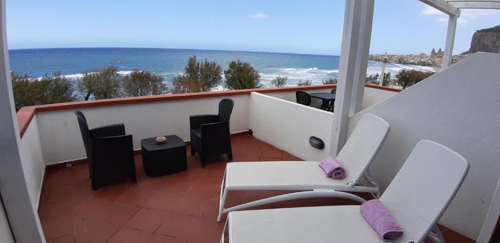 Un balcón con sillas blancas y vistas al océano. en Villa Cerniglia Plus, en Cefalú