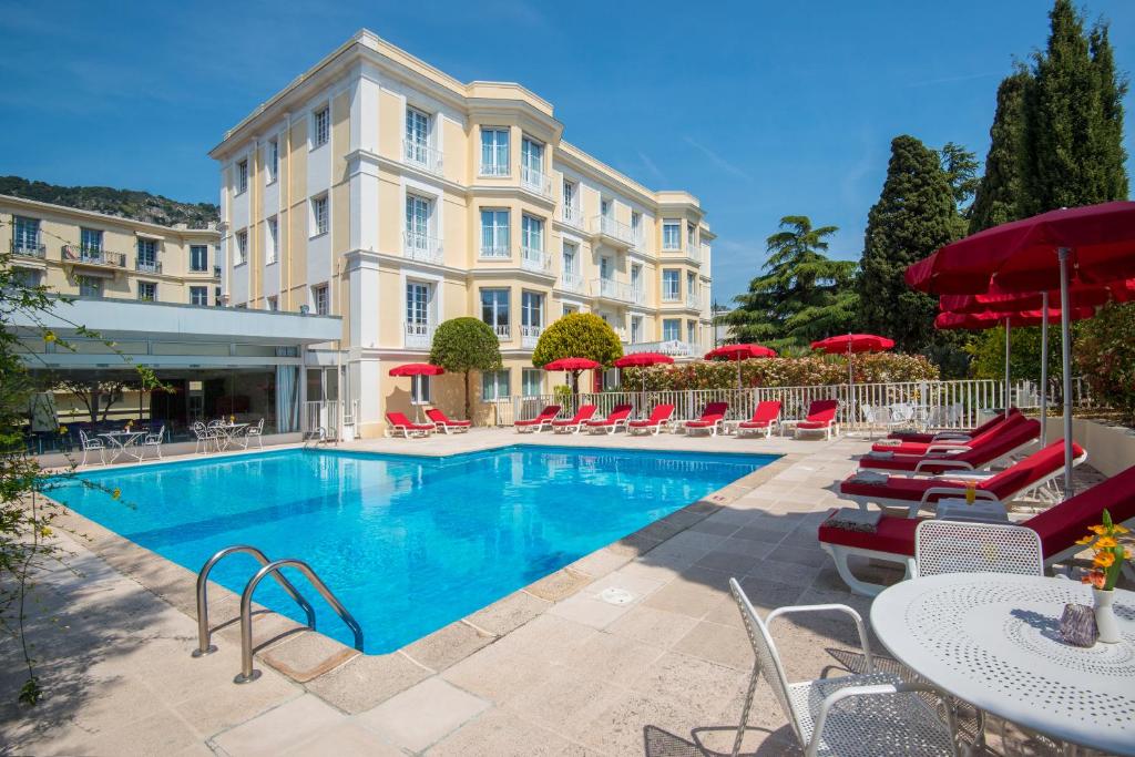 une piscine avec des chaises, des tables et des parasols rouges dans l'établissement Hotel Carlton, à Beaulieu-sur-Mer